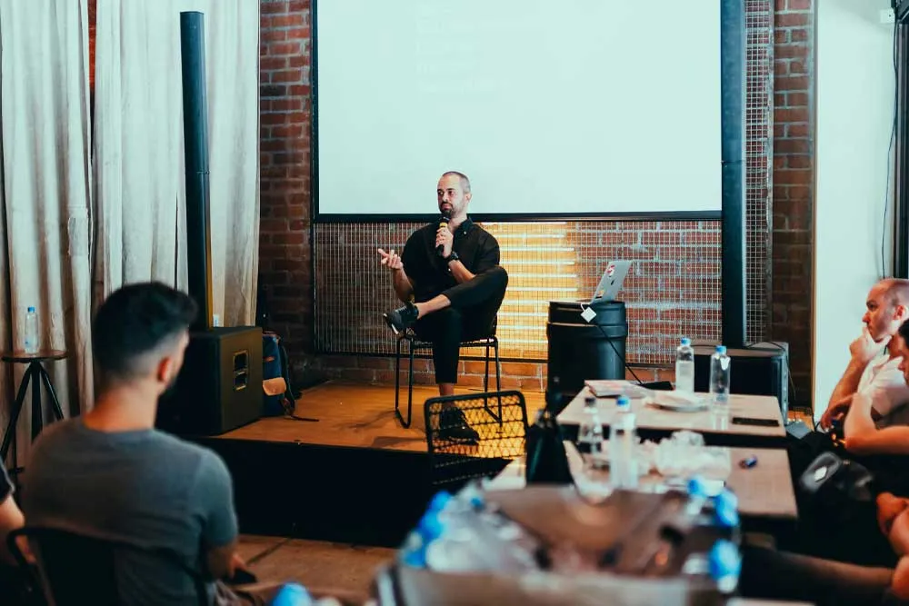 Ein Mann sitzt auf einer kleinen Bühne und die Teilnehmer in U-Besuthlung davor