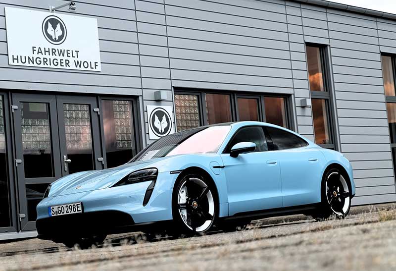 Porsche Taycan in blau vor dem Gebäude der Fahrwelt Hungriger Wolf