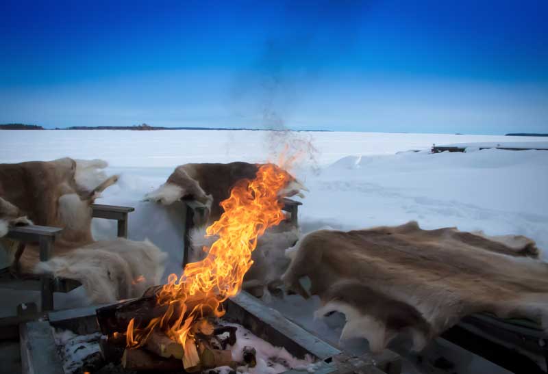 Feuerstelle im Schnee mit Sitzgelegeneheiten in Schwedisch Lappland