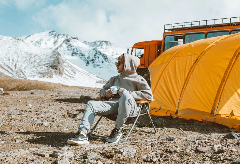 Influencer trinkt einen Kaffee vor seinem Zelt im Gebirge
